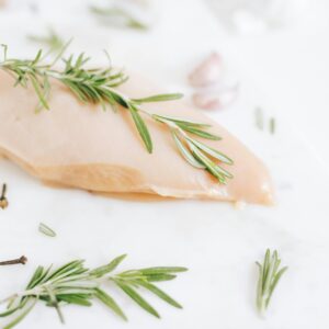 Healthy raw chicken breast garnished with rosemary on a marble surface.