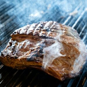 A sizzling juicy steak on a BBQ grill with visible smoke, perfect for summer barbecue themes.