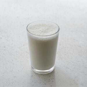 A frothy glass of milk on a textured white surface, captured with minimalism.