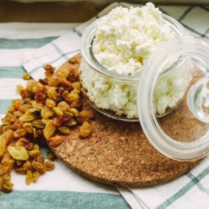 A close-up of cottage cheese in an open glass jar with scattered raisins on a cloth surface.