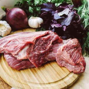 Close-up of raw beef on a wooden board with fresh herbs and vegetables.